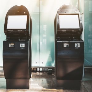 Two black electronic check-in counters in the departure area of the airport terminal or railway station depot with empty white screen mockups; templates of blank LCD screens of self-service terminals